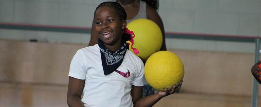 Girl holding ball in gym smiling.