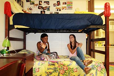 Two female students sitting on bed in dorm