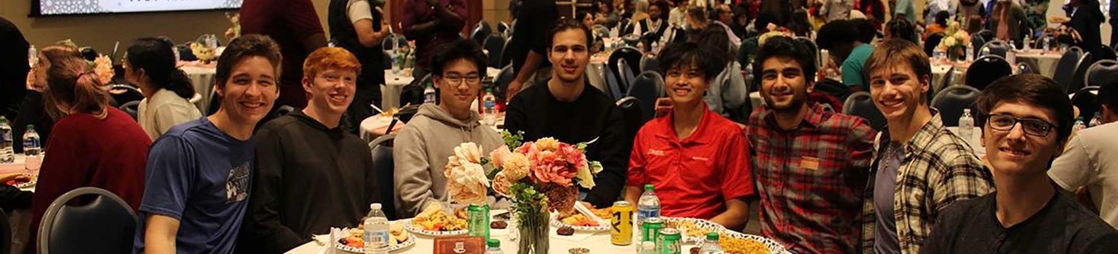 Group of 学生 sitting at a round table eating at event.